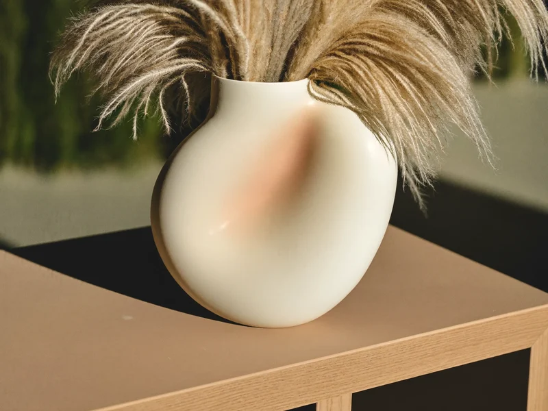 Matte cremefarbene Keramikvase mit Trockengras auf einer Konsole aus heller Eiche