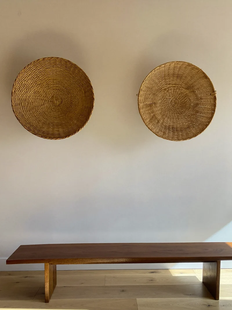 Zwei runde Rattan-Wandstücke über einer kleinen Holzbank an heller Putzwand